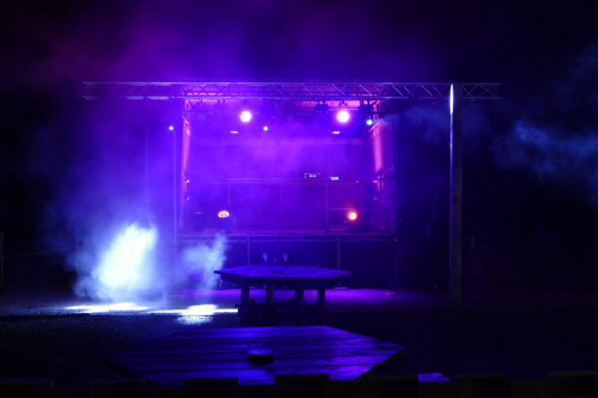 Outdoor stage setup illuminated with vibrant purple lighting and smoke effects, ideal for concerts or live events.