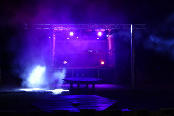Outdoor stage setup illuminated with vibrant purple lighting and smoke effects, ideal for concerts or live events.