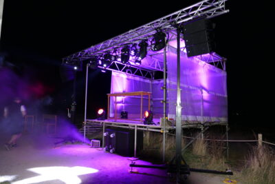 Outdoor stage setup with purple lighting, featuring truss system and sound speakers, prepared for a night event or concert.