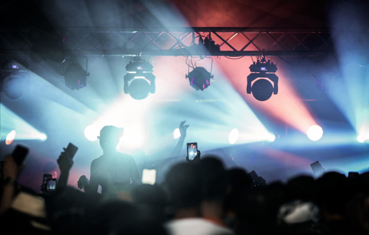 Concert scene with dynamic stage lighting and silhouettes of the audience capturing the event on phones.