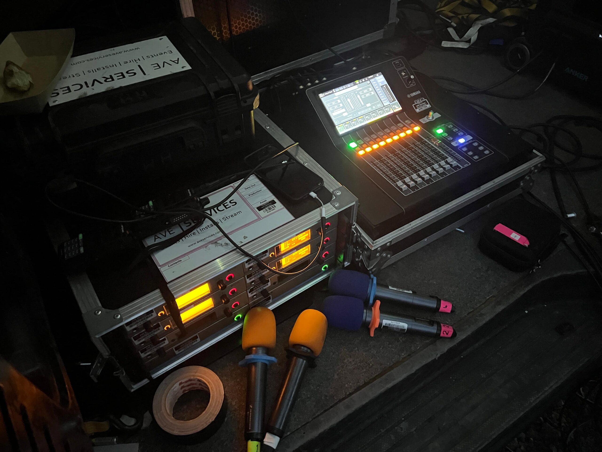 Audio mixing station with illuminated soundboard and wireless microphones, ready for live event production setup.