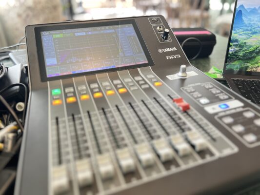 Audio mixing console with digital interface, featuring sliders and control knobs, used for live event sound management.