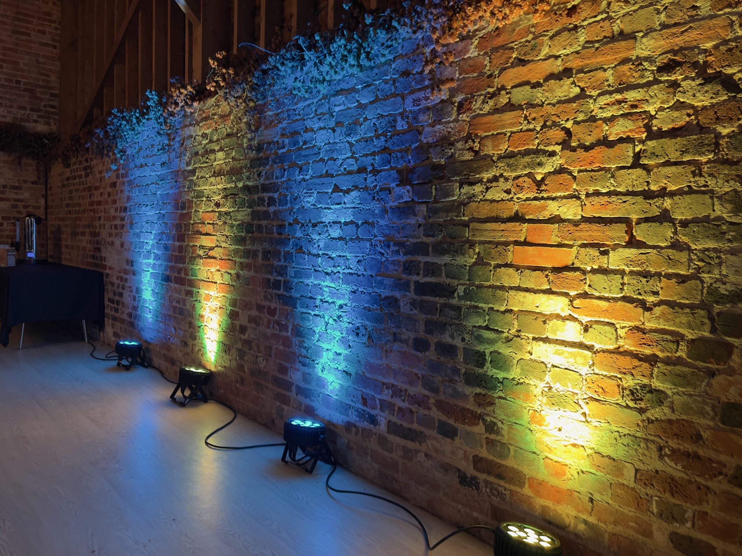 Uplighting illuminates a rustic brick wall with colorful beams, ideal for weddings or corporate events.